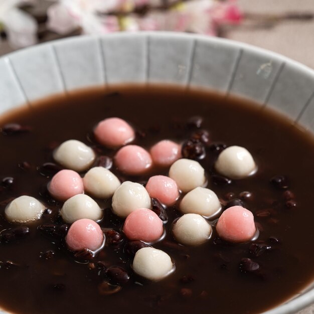 Feche de tangyuan vermelho e branco (tang yuan, bolas de bolinho de arroz glutinoso) com sopa de feijão vermelho doce em uma tigela no fundo da mesa cinza para comida do festival do solstício de inverno.