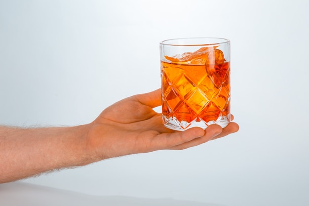 Feche de uma mão segurando um copo de negroni cocktail em branco com espaço de cópia.