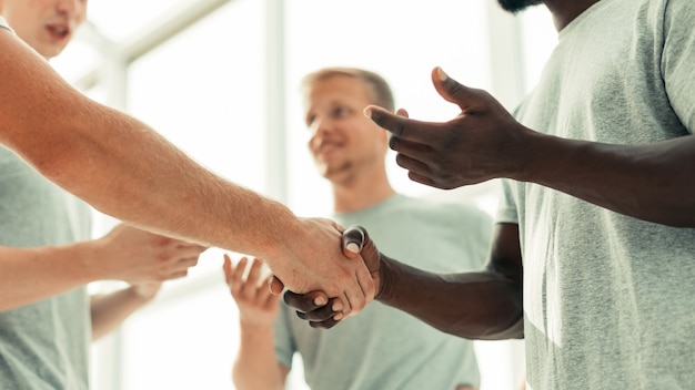 Foto feche dois camaradas apertando as mãos em um círculo de amigos