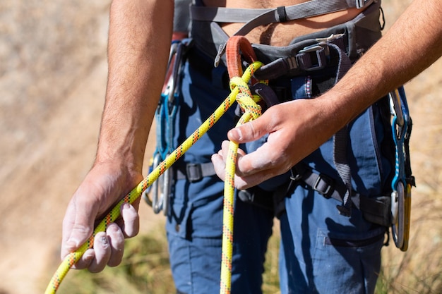 Feche o alpinista fazendo um nó chamado duplo oito com a corda no arnês