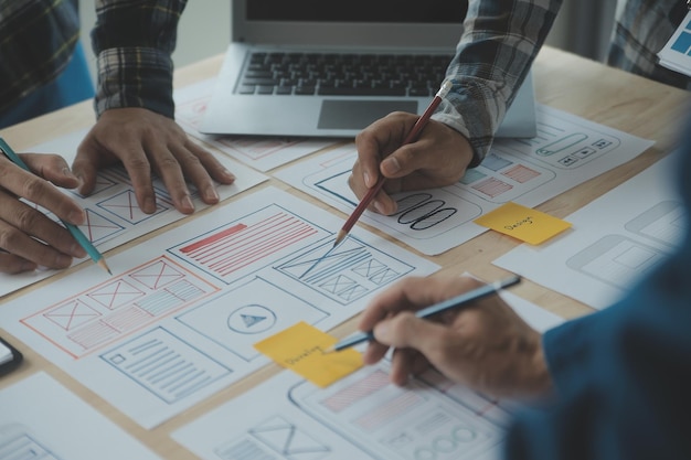 Feche o brainstorming do desenvolvedor de ux e do designer de interface do usuário sobre o design de wireframe da interface de aplicativo móvel na mesa com resumo do cliente e código de cores no escritório modernoAgência de desenvolvimento digital criativo