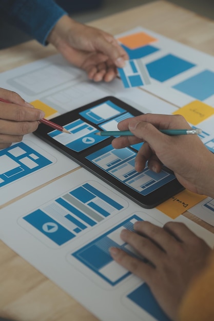 Feche o brainstorming do desenvolvedor de ux e do designer de interface do usuário sobre o design de wireframe da interface de aplicativo móvel na mesa com resumo do cliente e código de cores no escritório modernoAgência de desenvolvimento digital criativo