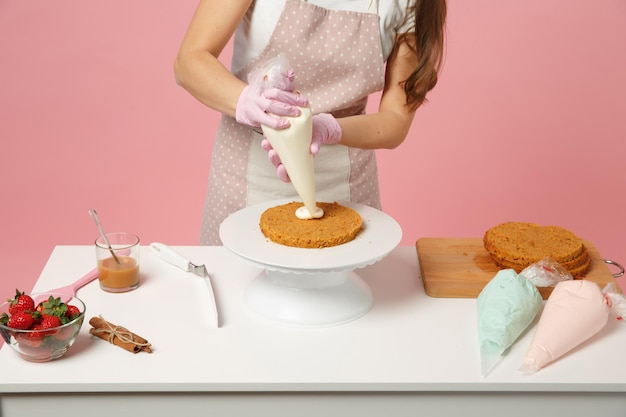 Foto feche o chef recortado cozinhar confeiteiro ou padeiro em camiseta branca cozinhando na mesa isolada em fundo rosa pastel no estúdio. processo de fabricação de bolo de aplicação de creme. mock up conceito de comida de espaço de cópia.