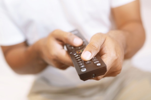 Feche o controle remoto da televisão nas mãos de um homem casual, apontando para o aparelho de TV e ligando ou desligando-o. selecione o canal assistindo tv em seu sofá em casa na sala relaxar.