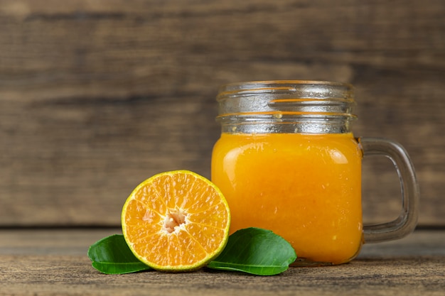 Feche o corte da laranja ao meio e um copo de suco de laranja na parede da mesa de madeira.