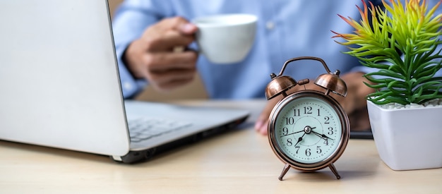 Foto feche o despertador com o jovem empresário usando laptop