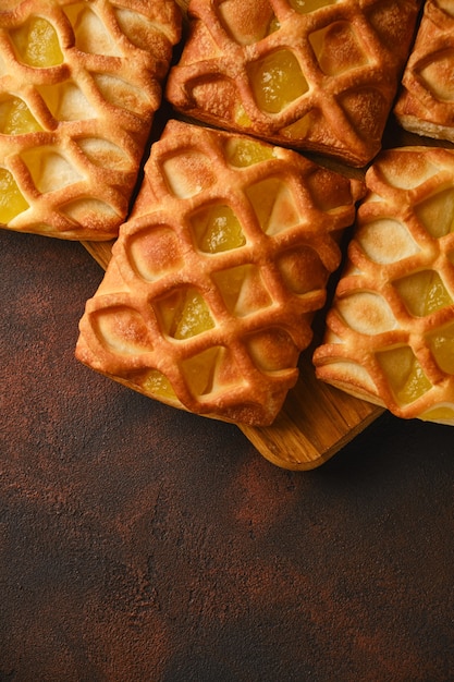 Feche o fundo de mini tortas de massa folhada crocante fresca com recheio de geleia de pêra e limão Em um plano de fundo texturizado preto e vermelho escuro com fatias de pêra e limão frescas, de cima, flatlay