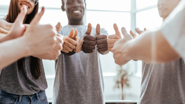 Feche o grupo de jovens formando um círculo e mostrando os polegares para cima