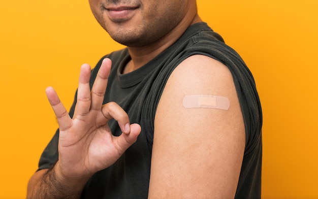 Feche o homem asiático vacinado mostrando o braço após o coronavírus Vacinação isolada de fundo amarelo Homem indiano mostra sinal de ok e recebendo uma imunização covid19 de vacinação