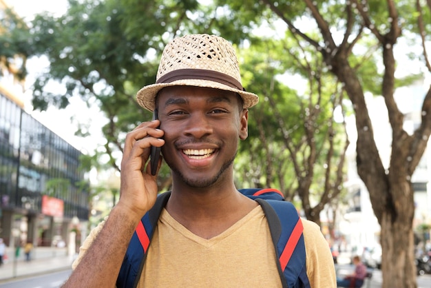 Feche o homem negro sorridente com chapéu falando no celular