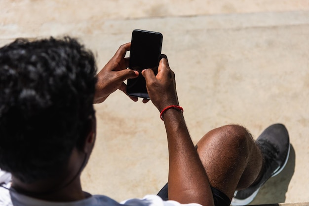 Feche o jovem atleta asiático, corredor esportivo, homem negro, use relógio inteligente moderno e sincronize com um smartphone, verifique o resultado da corrida após o treinamento executado ao ar livre, tecnologia de exercícios saudáveis