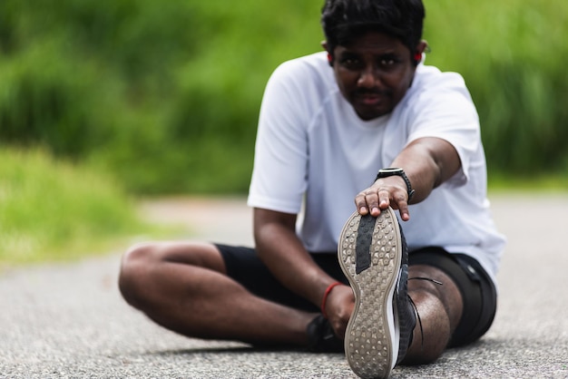 Feche o jovem atleta asiático, corredor esportivo, o homem negro usa relógio sentado puxando os pés esticando as pernas e o joelho antes de correr no parque de saúde de rua ao ar livre, exercício saudável antes do conceito de treino