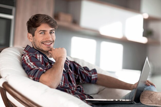 Feche o jovem bem sucedido sentado na frente de um laptop aberto