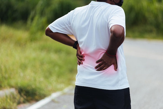 Feche o jovem corredor esportivo asiático, o homem negro usa relógio, sente dor na coluna lombar e no quadril enquanto corre no parque de saúde de rua ao ar livre, exercício saudável Lesão do conceito de treino