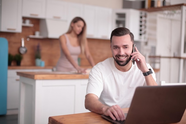 Feche o jovem falando no smartphone na cozinha de casa