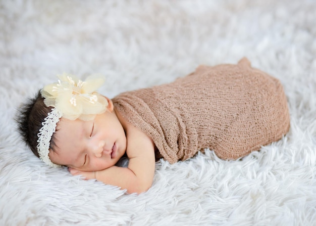 Feche o lindo recém-nascido usando faixa de flor em tapetes de lã, conceito de moda