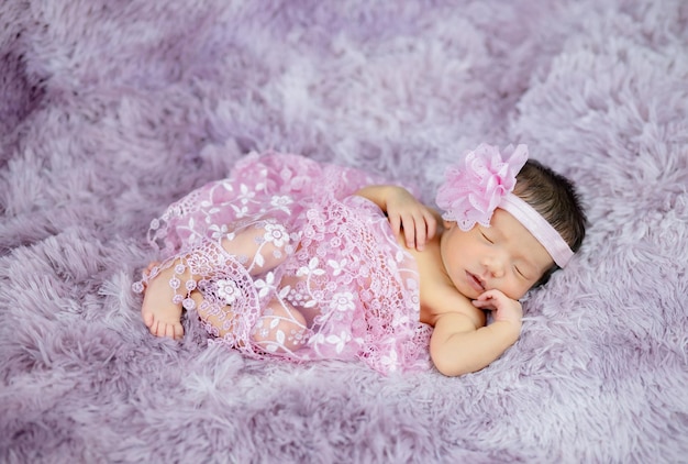 Feche o lindo recém-nascido usando faixa de flor em tapetes de lã roxos, conceito de moda