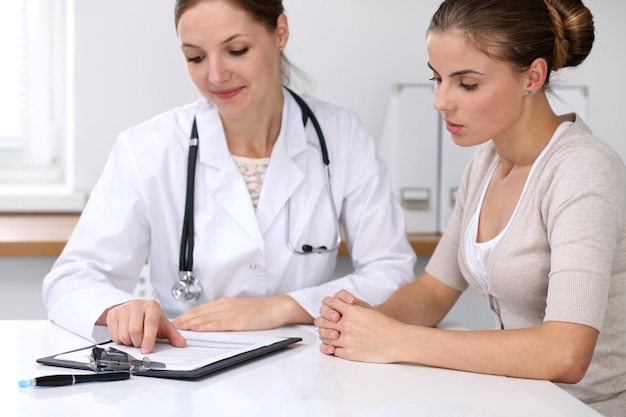 Feche o médico e o paciente sentados à mesa enquanto o médico aponta para a história do formulário médico. conceito de medicina e cuidados de saúde