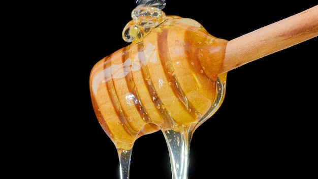 Feche o mel fluido fresco derramando e fluindo da colher de concha de madeira