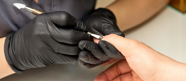 Feche o mestre manicure profissional segurando a mão do cliente enquanto usa um empurrador de cutícula em um salão de beleza