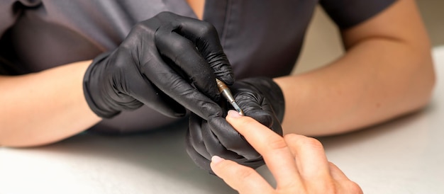 Feche o mestre manicure profissional segurando a mão do cliente enquanto usa um empurrador de cutícula em um salão de beleza