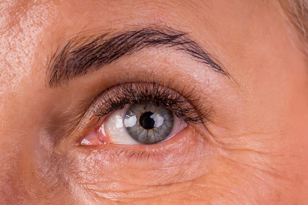 Feche o olho azul da velha com sobrancelhas decoradas arrancadas e extensões conceito de identificação de cílios longos.