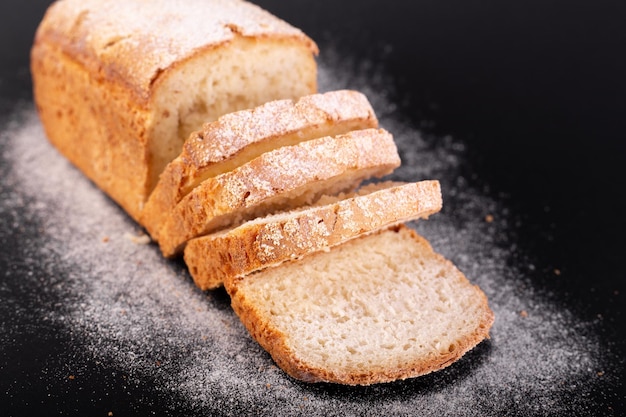 Feche o pão magro francês fatiado com farinha em um fundo preto Receita de conceito de pão artesanal