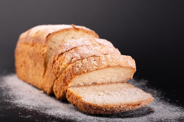 Feche o pão magro francês fatiado com farinha em um fundo preto receita de conceito de pão artesanal