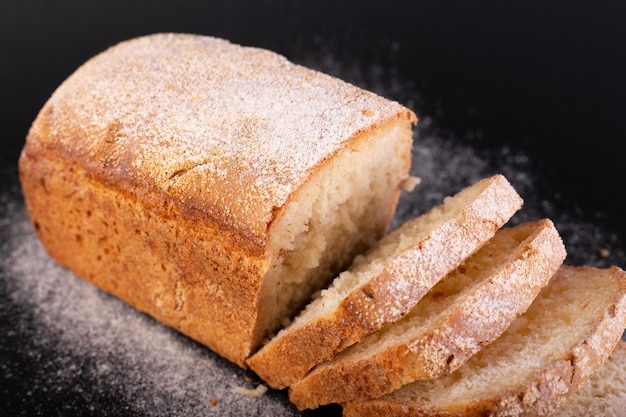 Feche o pão magro francês fatiado com farinha em um fundo preto Receita de conceito de pão artesanal