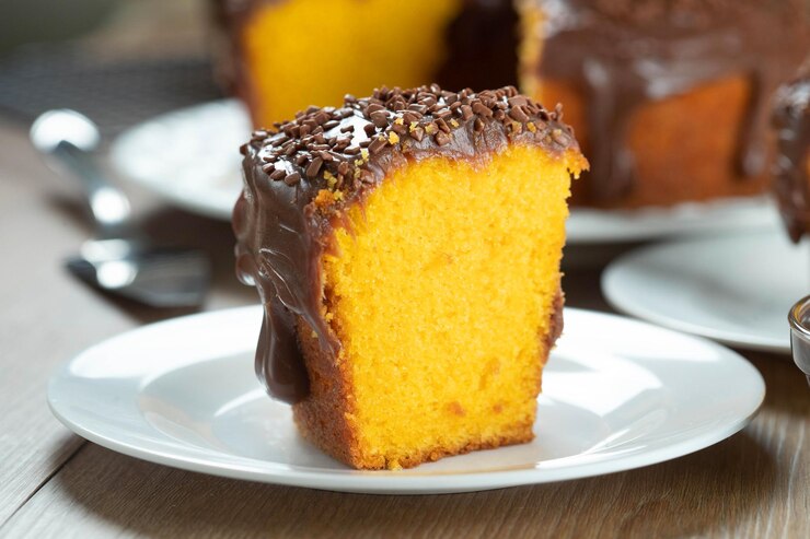 Foto feche o pedaço de bolo de cenoura brasileiro com cobertura de chocolate na mesa de madeira com cenouras ao fundo