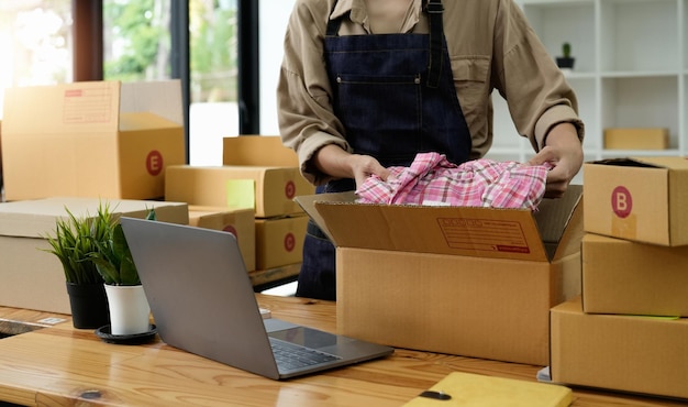 Feche o proprietário do jovem empresário embalando roupas para a caixa de papelão Jovem Proprietário Mulher Start-up para negócios on-line Pessoas com compras on-line empresário PME ou conceito de trabalho freelance