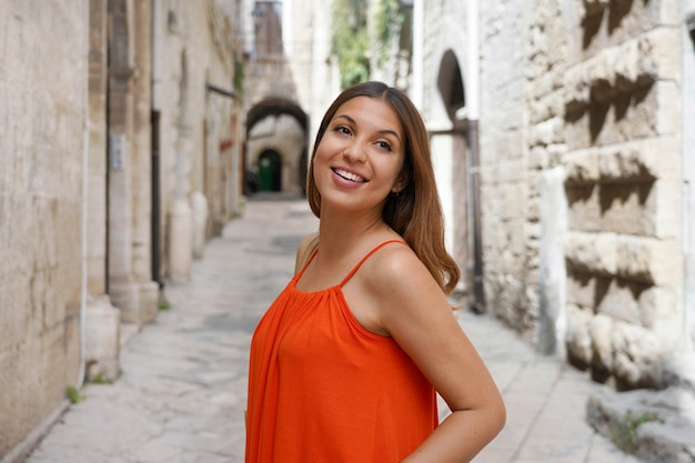 Feche o retrato ao ar livre de uma linda mulher em um vestido laranja, se virando enquanto caminha pela histórica cidade medieval