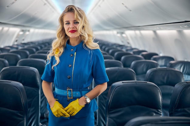 Feche o retrato da aeromoça sorridente e feliz em uniforme azul, posando para a câmera fotográfica em um moderno avião de passageiros