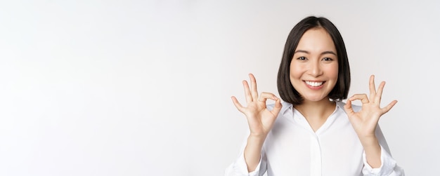 Feche o retrato da cabeça de uma garota asiática mostrando sinal de ok e sorrindo satisfeito recomendando ser p