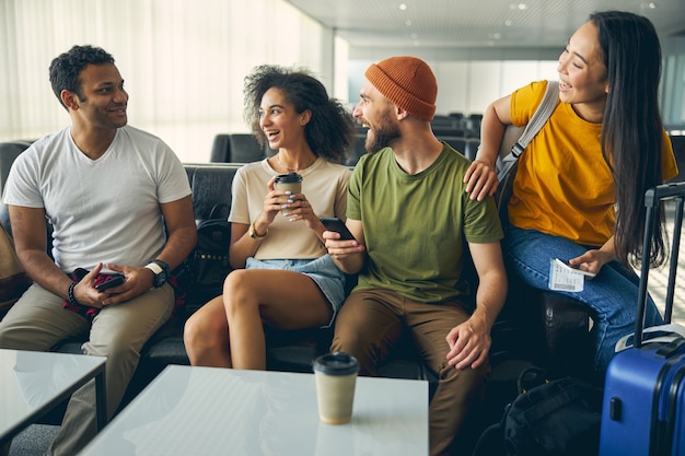 Feche o retrato da equipe amigável feliz em roupas elegantes engraçadas na sala de embarque do aeroporto