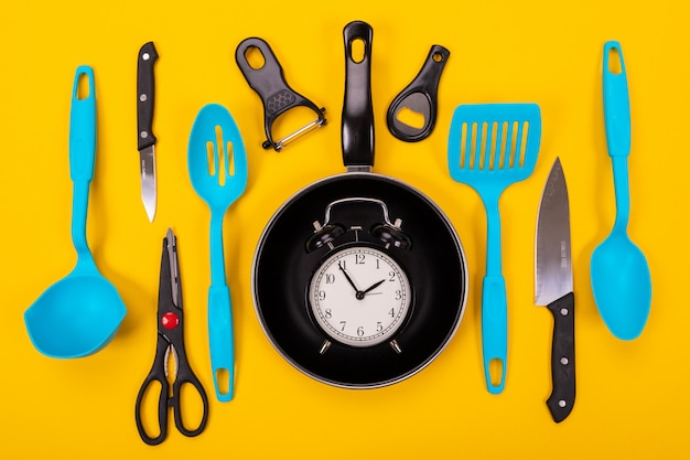 Feche o retrato da frigideira com conjunto de utensílios de cozinha em fundo amarelo