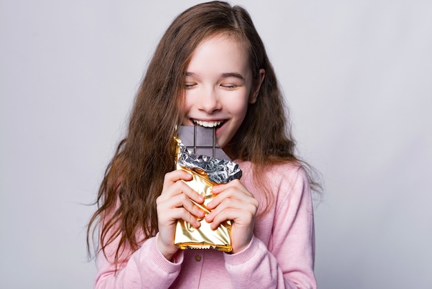 Feche o retrato da linda garota comendo chocolate sobre cinza e sorria