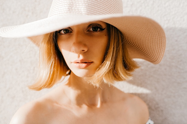 Foto feche o retrato da menina loira elegante de cabelo curto com chapéu posando sobre branco