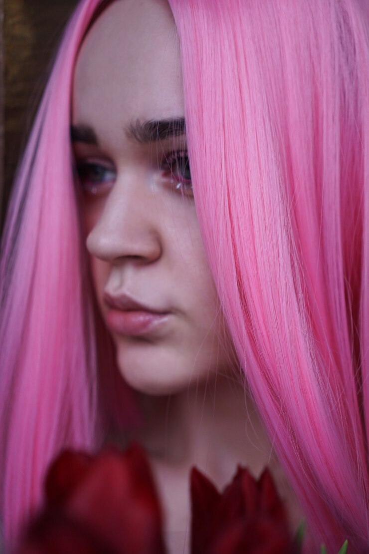 Foto feche o retrato da moda. foto vertical. retrato de uma menina sonhadora com cabelo rosa brilhante com flores perto do rosto. olhando para o lado