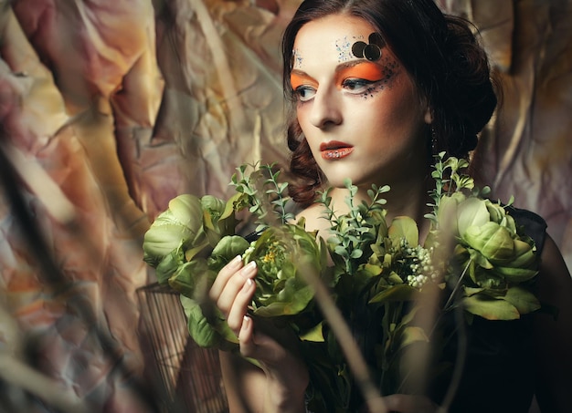 Feche o retrato da mulher ruiva com maquiagem criativa brilhante segurando flores secas