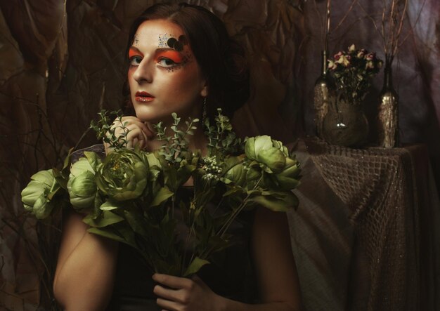 Feche o retrato da mulher ruiva com maquiagem criativa brilhante segurando flores secas