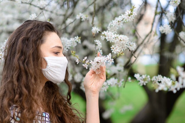 Feche o retrato da terna mulher sob uma cerejeira em flor com uma máscara