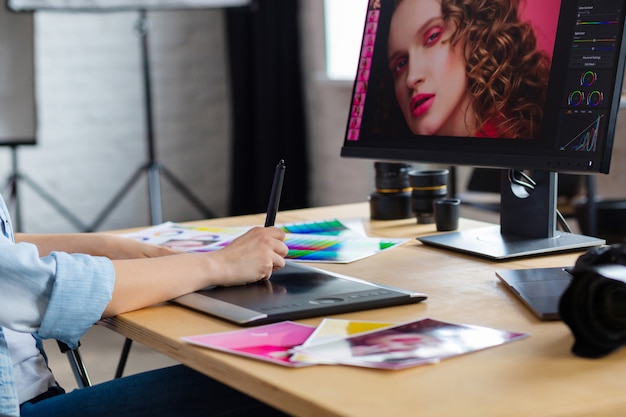 Foto feche o retrato das mãos do designer gráfico que retocam as imagens usando a tabuleta de desenho gráfico em programa especial.