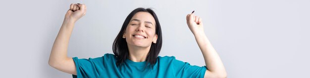 Feche o retrato de atraente gritando em vencer sorrindo com punhos levantados jovem ela sua garota vestindo roupas de camisa jeans isoladas em fundo cinza