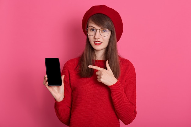 Feche o retrato de atraente mulher caucasiana, segurando o smartphone com tela em branco