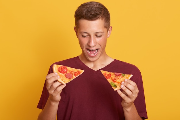 Feche o retrato de jovem estar pronto para comer uma deliciosa pizza isolada sobre amarelo