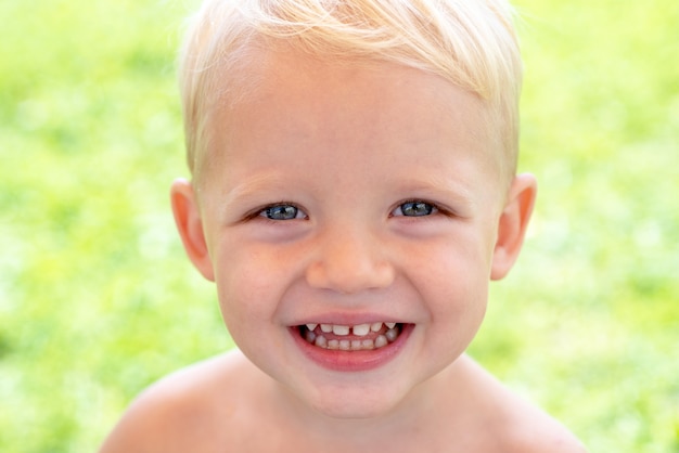 Feche o retrato de menino criança sorridente feliz no fundo verde da natureza