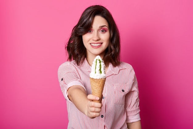 Foto feche o retrato de mulher bonita, oferecendo sorvete, senhora vestindo camisa listrada fica sorrindo