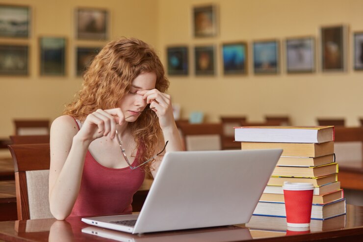 Feche o retrato de mulher triste axhuasted, sentindo-se cansado sentado à mesa na sala de leitura com laptop, estar com os óculos, mantém os dedos no nariz, parece infeliz. Conceito de educação e universidade.