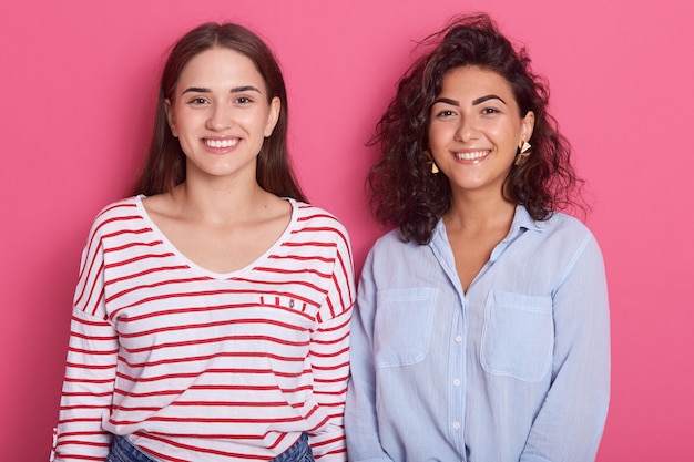 Feche o retrato de senhoras positivas em pé ao lado do outro, posando com um sorriso agradável